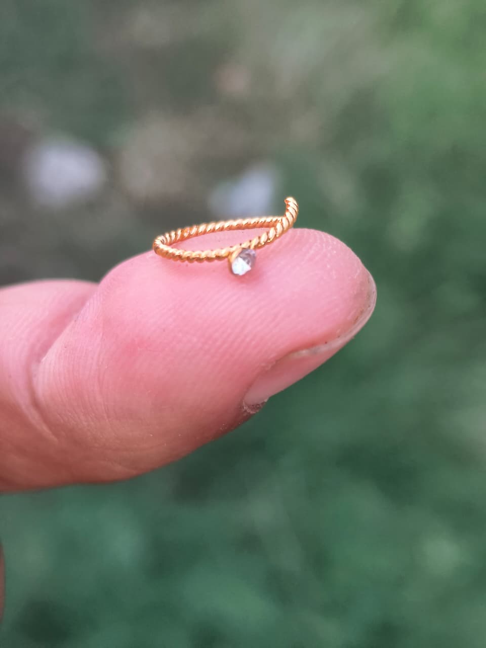 Gold ring with a small diamond on a finger against a blurred green background