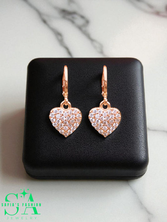 Heart-shaped earrings with rose gold finish and clear stones on a black jewelry box.