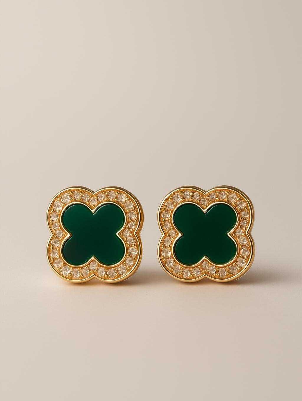 Pair of gold earrings with green clover-like stones on a beige background