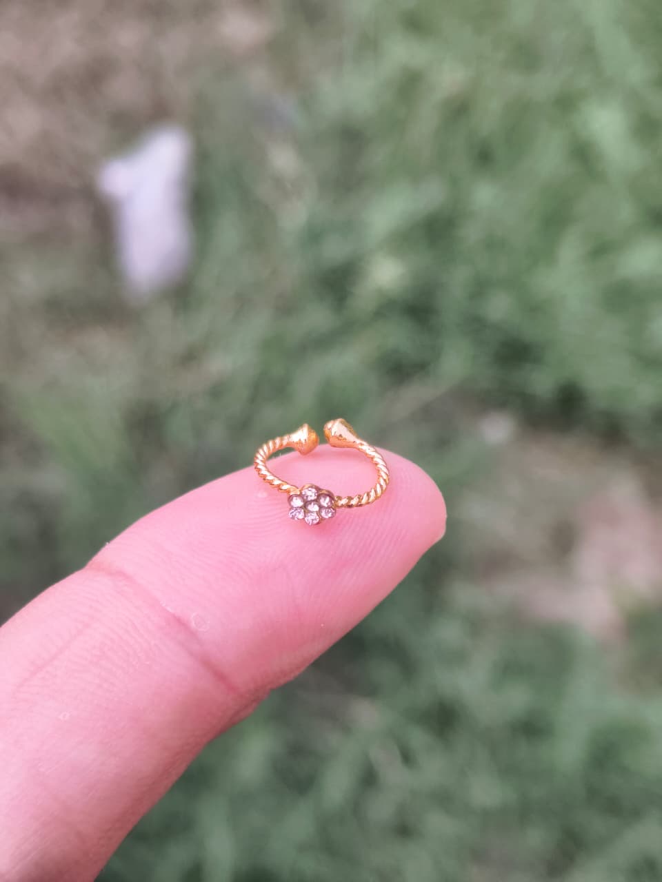 Gold ring with floral design on a finger against a blurred green background