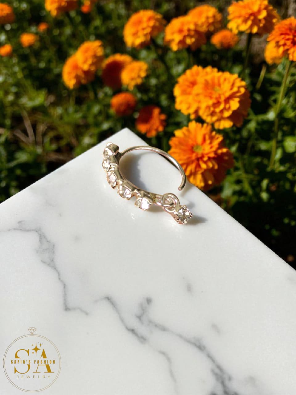 Gold ring with small stones on a marble surface with orange flowers in the background