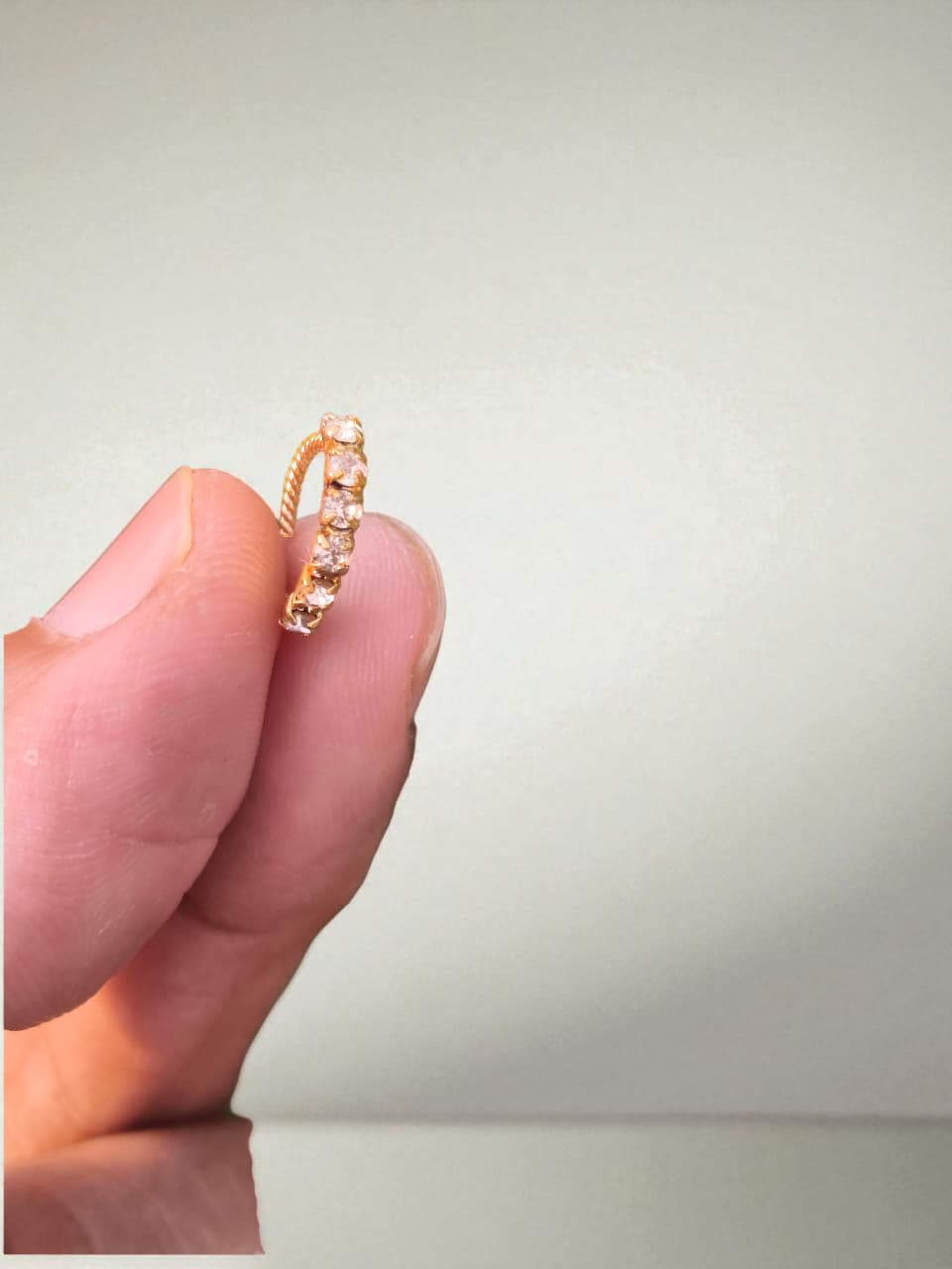 Gold ring with small stones held between fingers against a neutral background