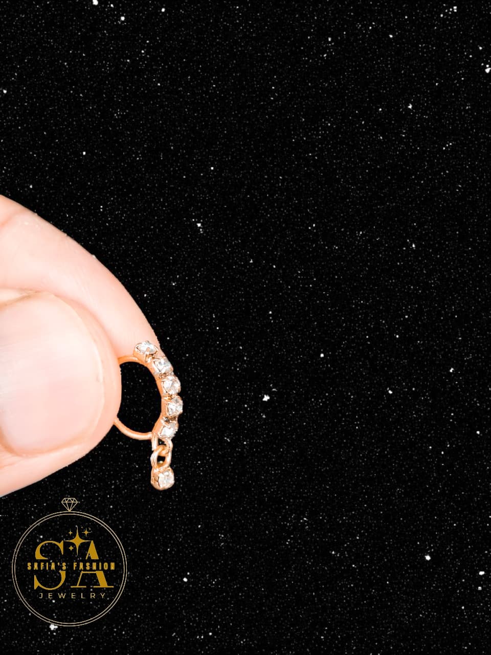 Gold earring with small stones held by a hand against a black background